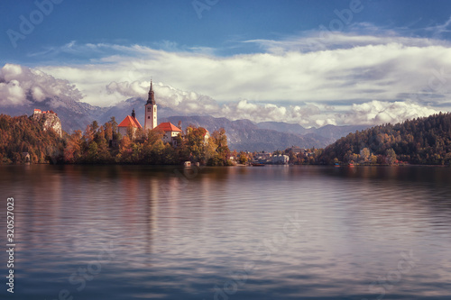 Famous alpine Bled lake (Blejsko jezero) in Slovenia, amazing autumn landscape. Scenic view of the lake, island with church, Bled castle, mountains and blue sky with clouds, outdoor travel background © larauhryn