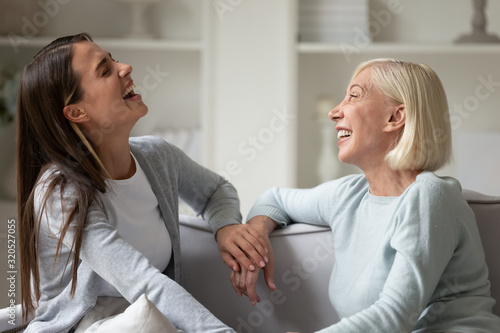 Overjoyed senior mom and adult daughter laugh talking at home