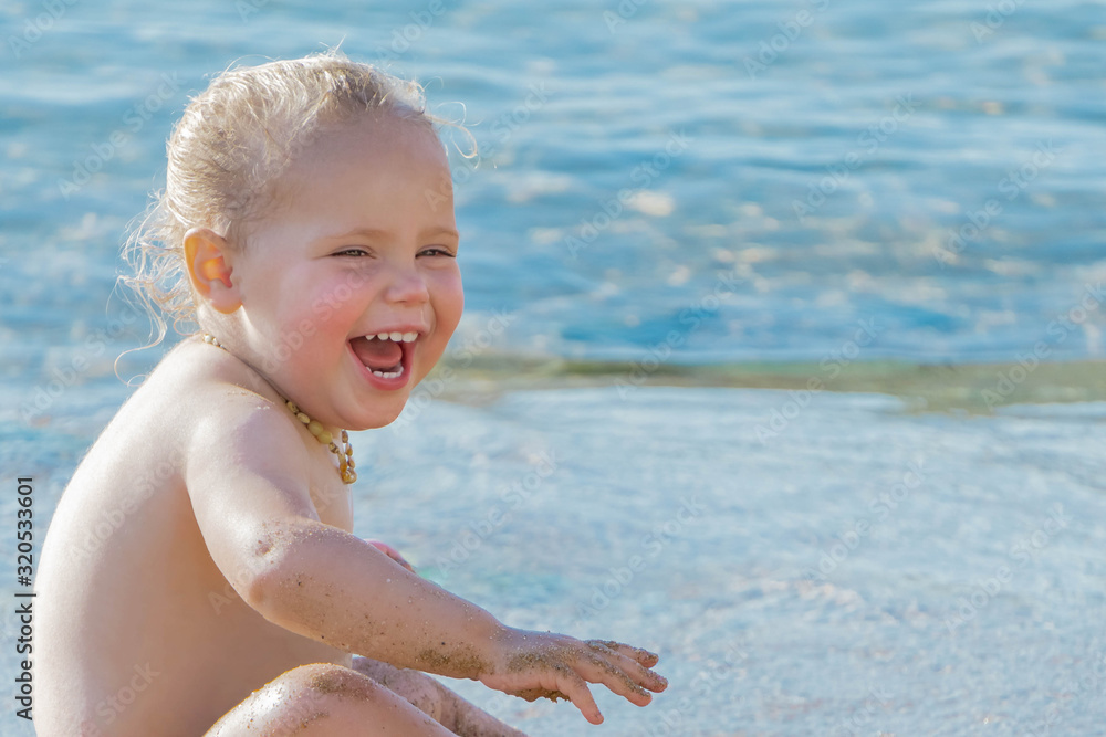 Happy toddler girl laughing and playing in sandy beach on sea background Happy toddler girl laughing and playing in sandy beach on sea background