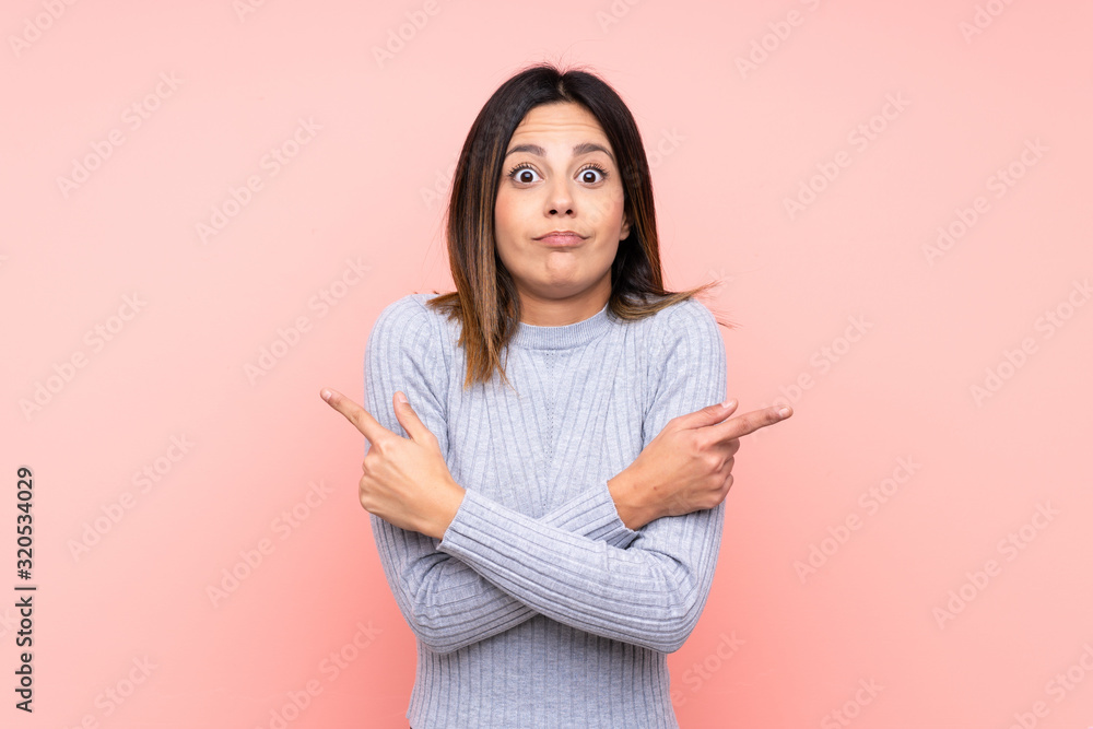 Fototapeta premium Woman over isolated pink background pointing to the laterals having doubts