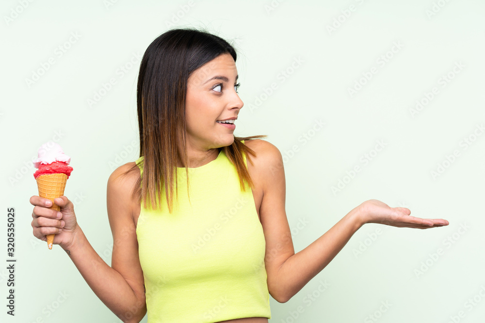 Brunette woman holding a cornet ice cream over isolated green background with surprise facial expression Brunette woman holding a cornet ice cream over isolated green background with surprise facial expression