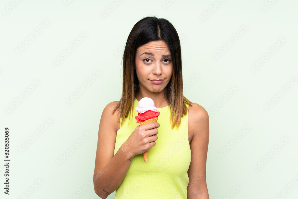 Brunette woman holding a cornet ice cream over isolated green background Brunette woman holding a cornet ice cream over isolated green background
