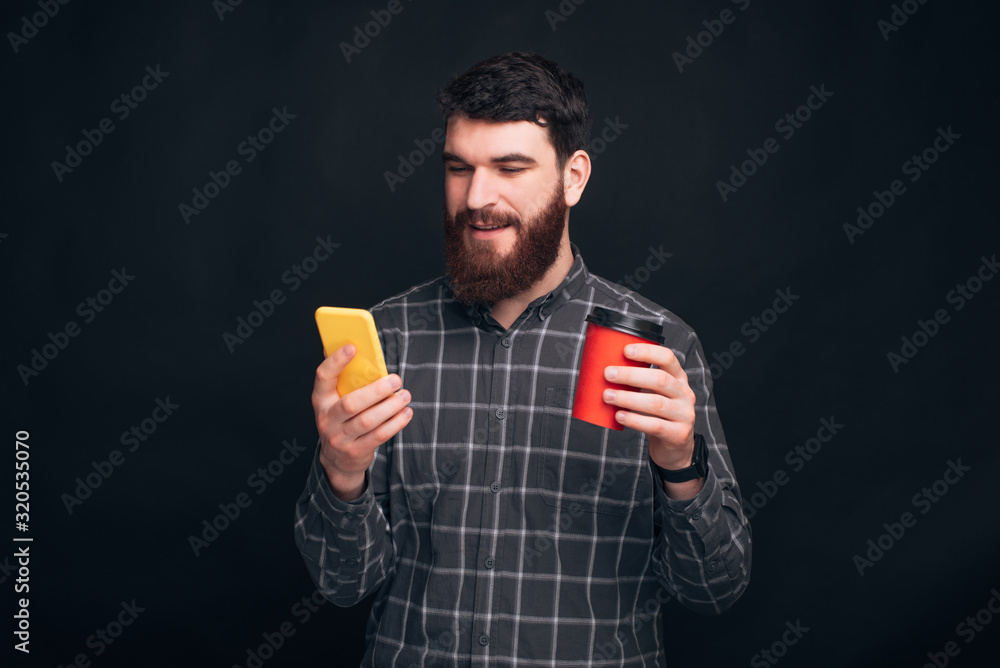 Have a great coffee break while surfing the internet. Youg student is looking at his phone and holding a take away cup. Have a great coffee break while surfing the internet. Youg student is looking at his phone and holding a take away cup.