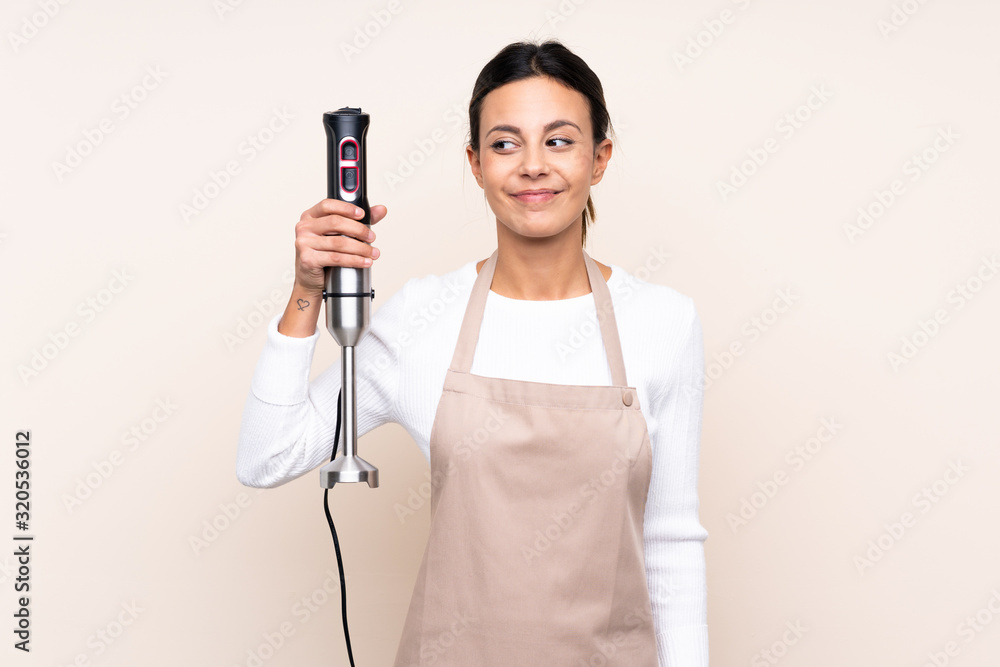 Woman using hand blender over isolated background with happy expression