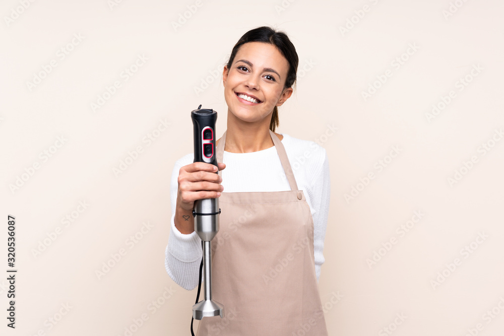 Woman using hand blender over isolated background with happy expression