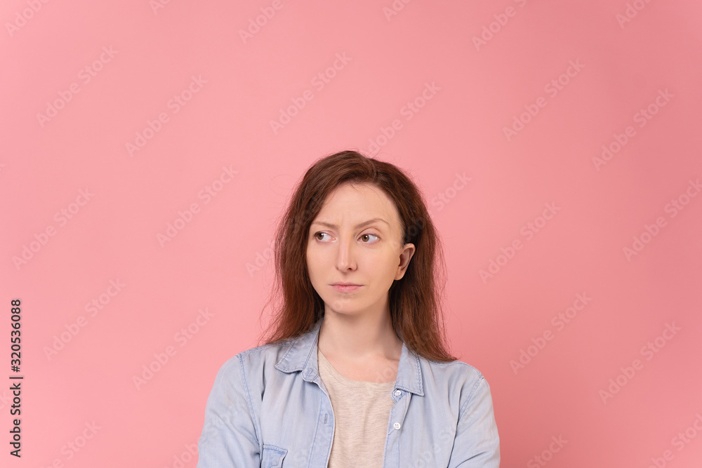 Young red-haired girl can not make a choice. Young female model has doubts about the solution to the problem. Distrust of others, bad mood. Uncertainty. Woman on a pink background Young red-haired girl can not make a choice. Young female model has doubts about the solution to the problem. Distrust of others, bad mood. Uncertainty. Woman on a pink background