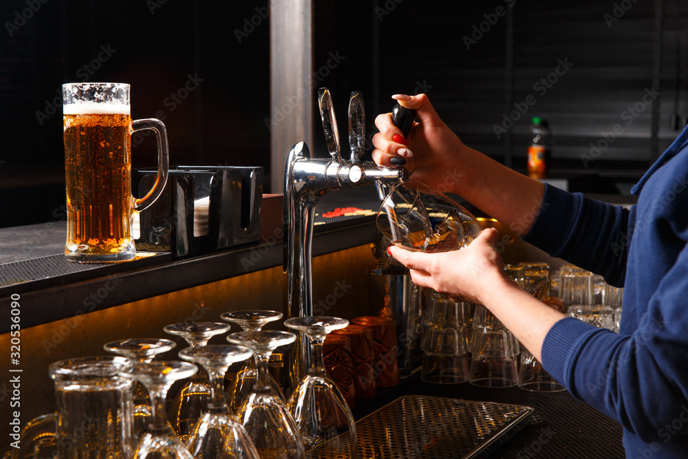 Hands of female bartender pouring from tap fresh beer into the glass in pub