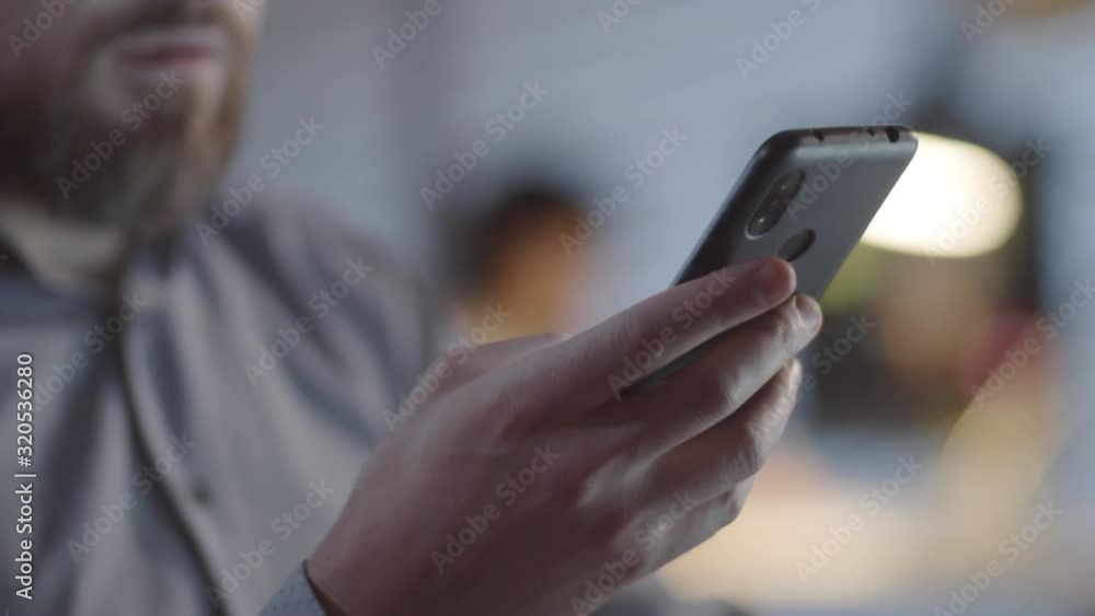 Close up shot of unrecognizable bearded man typing on mobile phone in dark office lit by lamplight Close up shot of unrecognizable bearded man typing on mobile phone in dark office lit by lamplight