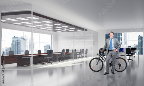 Smiling man in suit standing with bike in office