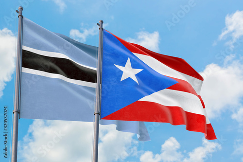 Puerto Rico and Botswana flags waving in the wind against white cloudy blue sky together. Diplomacy concept, international relations.
