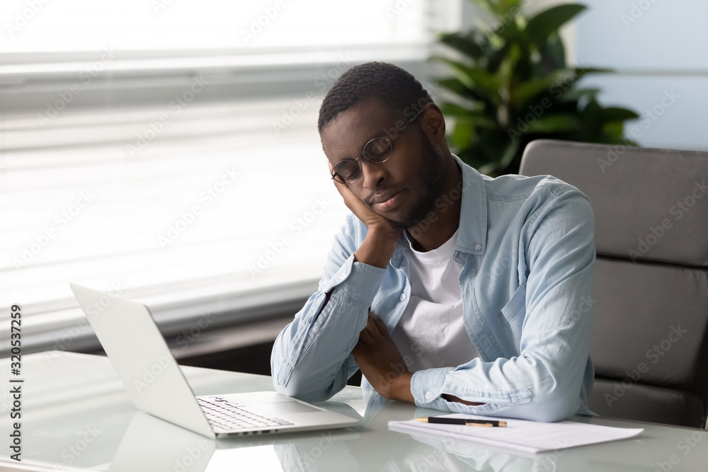 African employee falls asleep seated on chair at workplace African employee falls asleep seated on chair at workplace