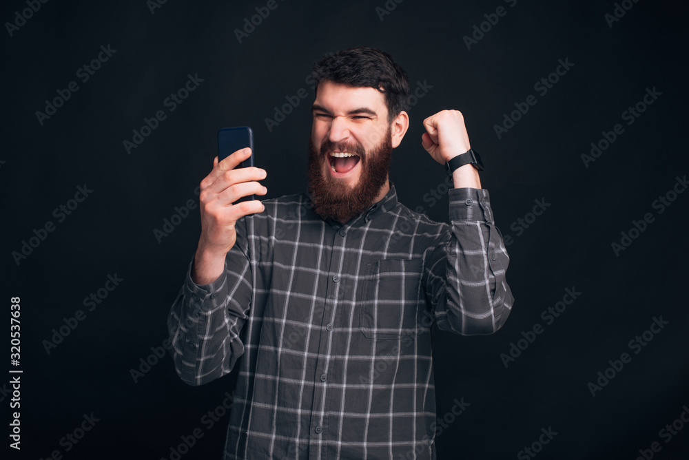 Oh , yes, i have won. Excited bearded man is looking at his phone and making the winner gesture with one arm. Oh , yes, i have won. Excited bearded man is looking at his phone and making the winner gesture with one arm.