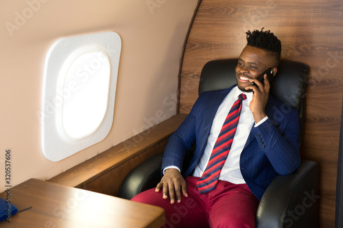 handsome african young man in a suit in the cabin of a private jet with a phone in his hand