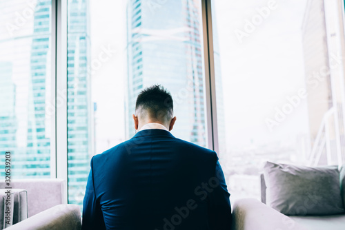 Anonymous male businessman in suit relaxing on armchair at office