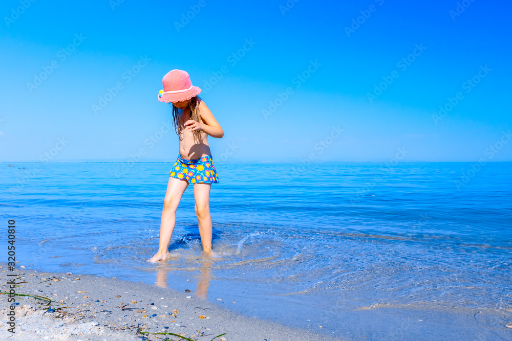 Child girl in summer straw hat is dancing happy barefoot in shallow sea water, beach Child girl in summer straw hat is dancing happy barefoot in shallow sea water, beach
