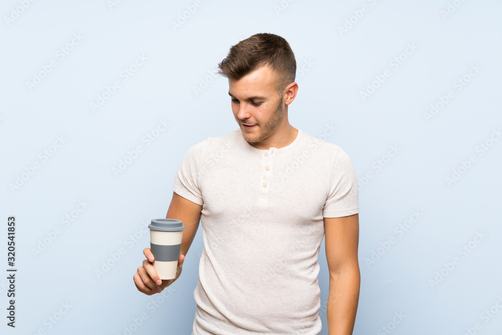 Young handsome blonde man over isolated blue background holding hot cup of coffee Young handsome blonde man over isolated blue background holding hot cup of coffee