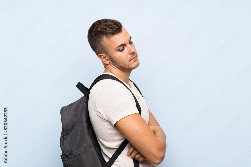 Young handsome blonde man over isolated blue background with backpack Young handsome blonde man over isolated blue background with backpack