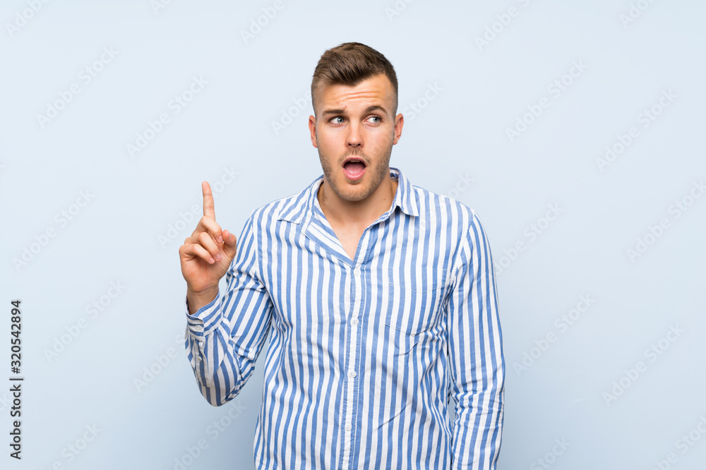Young handsome blonde man over isolated blue background thinking an idea pointing the finger up Young handsome blonde man over isolated blue background thinking an idea pointing the finger up