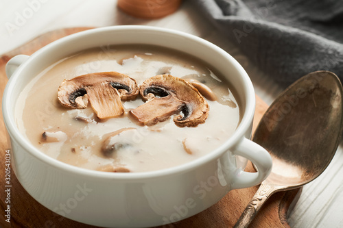 White bowl of mushroom soup on a cutting board and napkin on a white wooden background