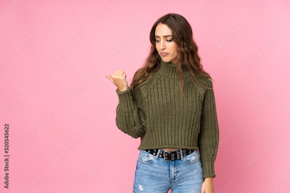 Young woman over isolated pink background unhappy and pointing to the side Young woman over isolated pink background unhappy and pointing to the side