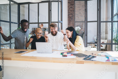Yelling cheerful multiethnic coworkers watching laptop in office