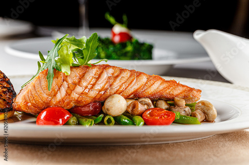 European cuisine. A large steak of red salmon fish, with mushrooms, asparagus, cherry tomatoes and fried lemon. Serving dishes in a restaurant on a white plate.