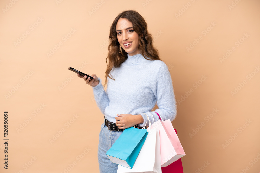 Young woman over isolated background holding shopping bags and writing a message with her cell phone to a friend Young woman over isolated background holding shopping bags and writing a message with her cell phone to a friend