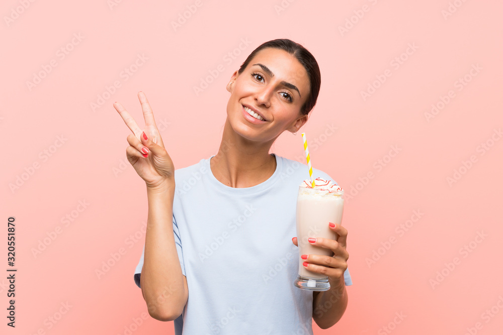 Young woman with strawberry milkshake over isolated pink background smiling and showing victory sign Young woman with strawberry milkshake over isolated pink background smiling and showing victory sign