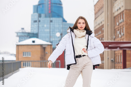 Fshion girl in a white down jacket and beige pants posing outdoors in winter