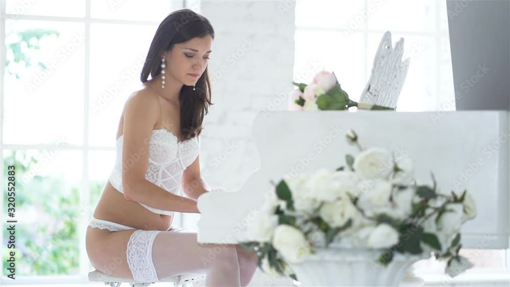 Portrait. Slow motion. Sexual young glamour woman in white lace lingerie plays piano Portrait. Slow motion. Sexual young glamour woman in white lace lingerie plays piano