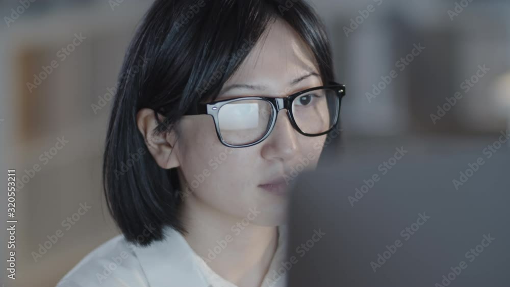 Tracking with close up of beautiful Asian woman in glasses and white blouse working on computer in dark office in evening Tracking with close up of beautiful Asian woman in glasses and white blouse working on computer in dark office in evening