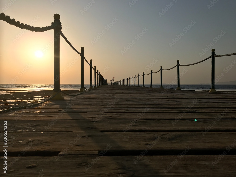 Sunrise in the morning on the seashore in Egypt. Wooden pier on a background of bright, summer rays. A large circle of the sun on the horizon over the Red Sea.