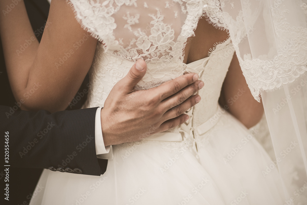 Closeup view photography of back of young bride and male hand of groom hugging waist of woman. Photo filtered in vintage sepia colors. Closeup view photography of back of young bride and male hand of groom hugging waist of woman. Photo filtered in vintage sepia colors.