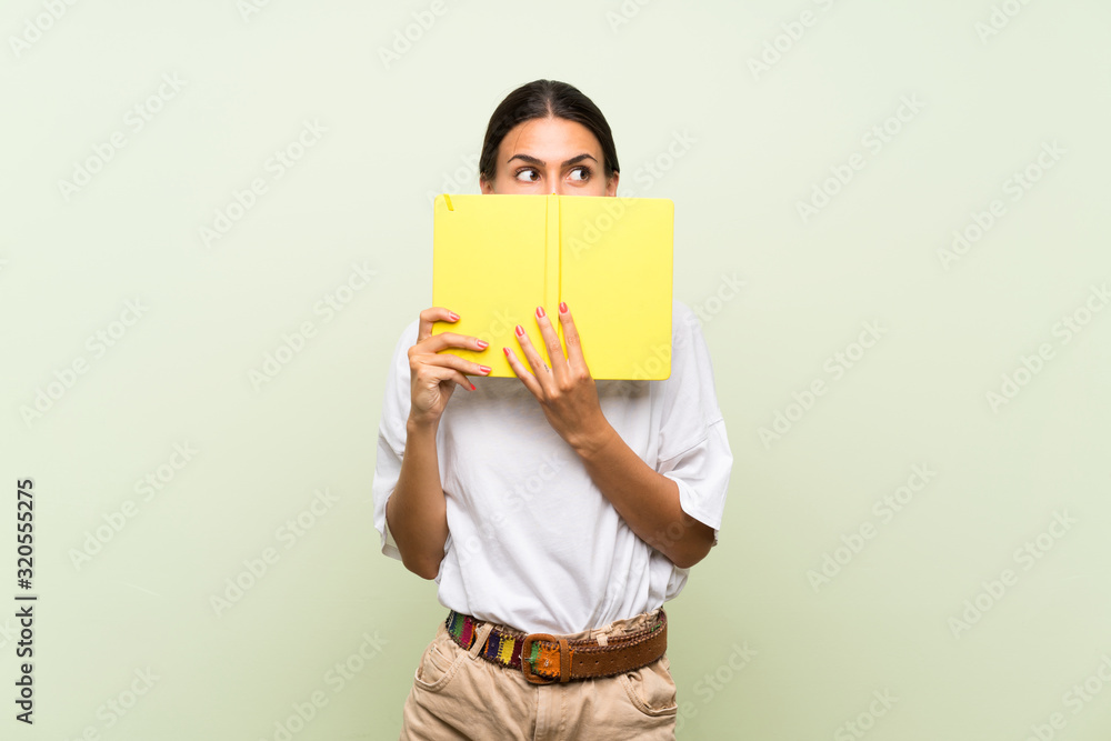 Young woman over isolated green background holding and reading a book Young woman over isolated green background holding and reading a book