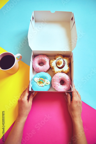 Sprinkled donuts in box and cup of coffee on colorful background.