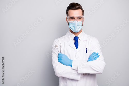 Close-up portrait of his he nice attractive cheerful experienced doc dentist holding in hands steel tools dental procedure center isolated on light white gray pastel color background photo