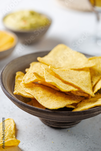 Nachos chips in a bowl with sauces and beer over white stone background.