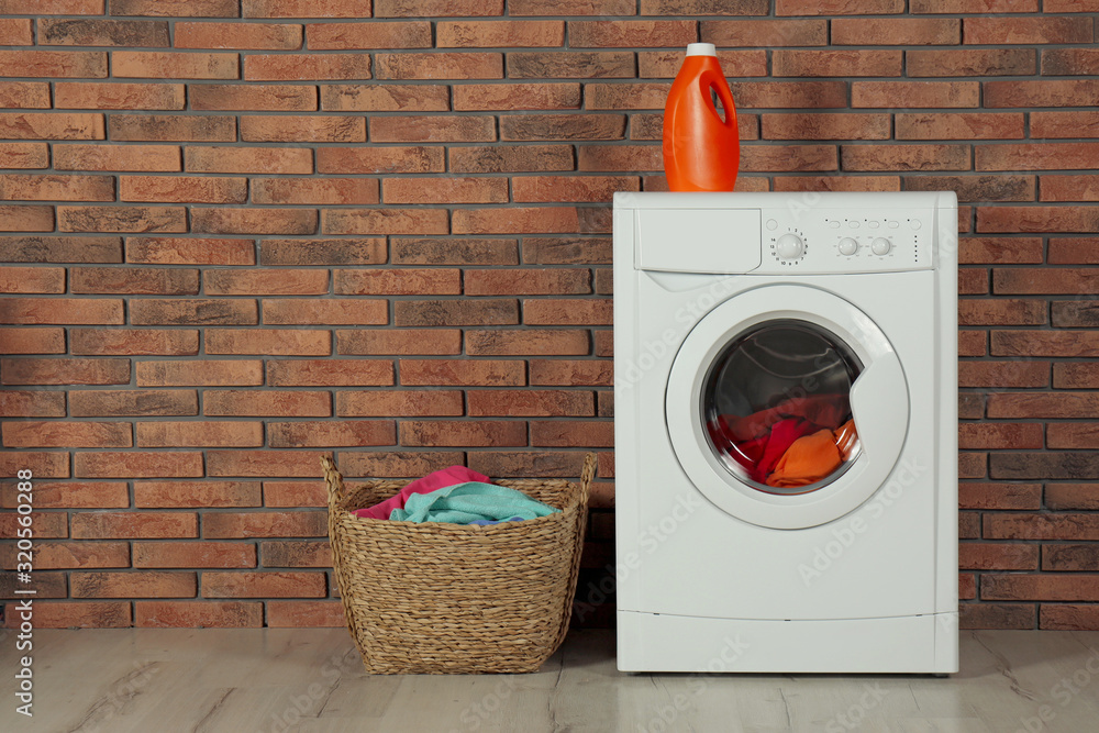 Modern washing machine with laundry, detergent and wicker basket near brick  wall. Space for text Stock Photo | Adobe Stock