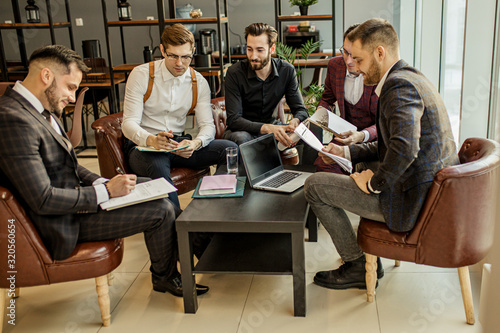 young caucasian business partners sharing and commenting reports. holding papers and notebooks, making notes and keep records of their market, in formal wear, isolated in modern office