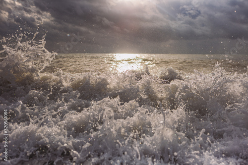 Beautiful dramatic awesome sea waves splashing at beach. Golden sunny sunset sky in background.