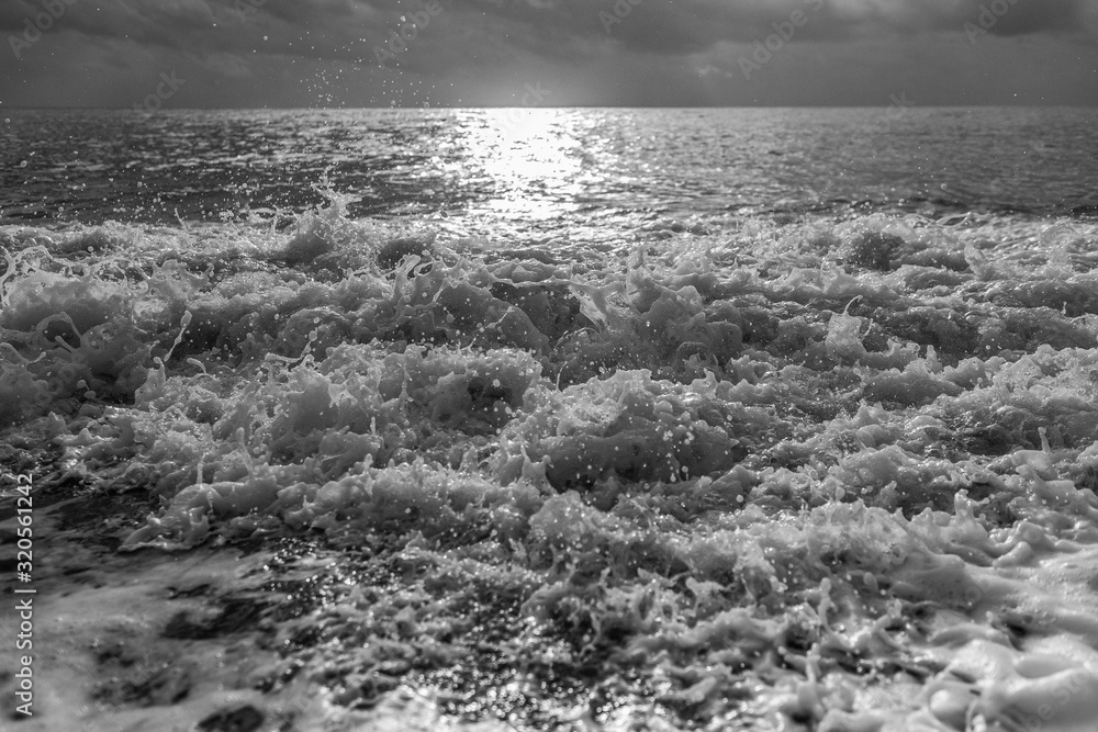Black and white photography of beautiful sunset or sunrise stormy sea waves splashing at seashore.
