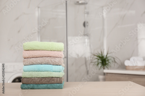 Stack of fresh towels on wooden table in bathroom. Space for text