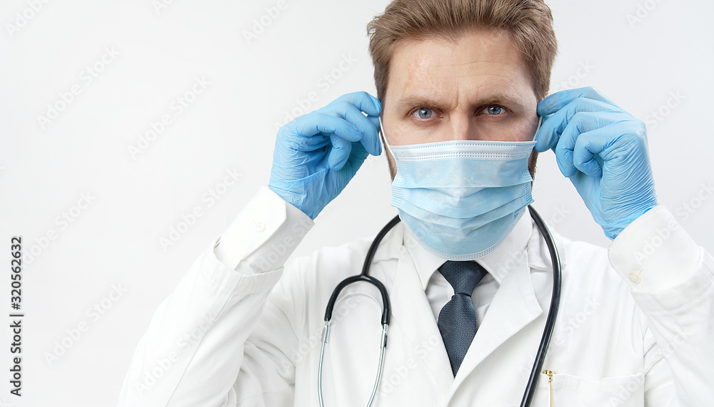 Potrait of practitioner putting on protective mask, having stethoscope, and blue surgical gloves while looking at camera isolated light background Potrait of practitioner putting on protective mask, having stethoscope, and blue surgical gloves while looking at camera isolated light background