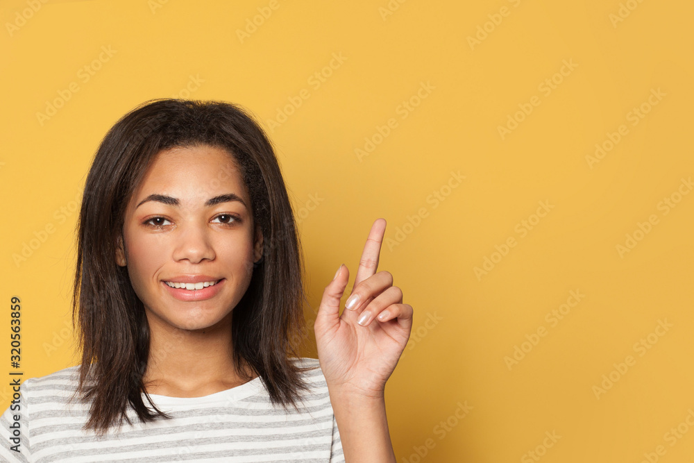 Young smart african american woman pointing up on vivid yellow studio background Young smart african american woman pointing up on vivid yellow studio background