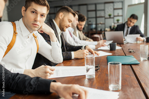 serious confident men in suits sit in office coworking, making notes, using papers. discuss and write business ideas