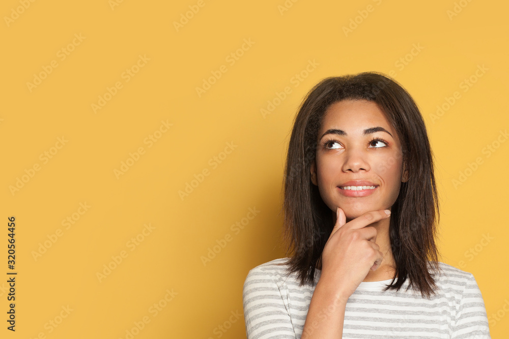Happy young black woman thinking on yellow background Happy young black woman thinking on yellow background