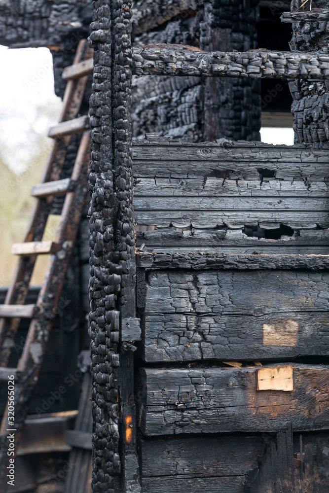 Charred boards of the interior walls of a room that burned in a fire with a staircase in the background.