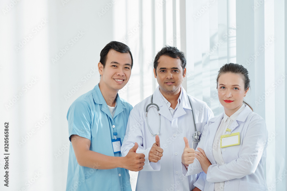 Happy healthcare workers in uniform and showing thumbs-up and smiling at camera Happy healthcare workers in uniform and showing thumbs-up and smiling at camera