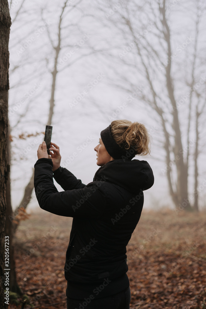 junge Frau im Wald macht Fotos mit ihrem Mobiltelefon im Herbst, moody Stil junge Frau im Wald macht Fotos mit ihrem Mobiltelefon im Herbst, moody Stil