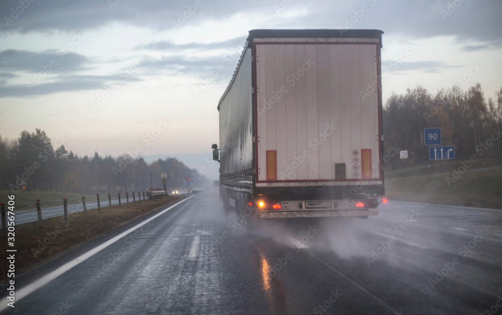 A truck with a trailer is being rebuilt on a motorway in a different row on slippery wet roads. The concept of security and attention to roads in bad weather, rain